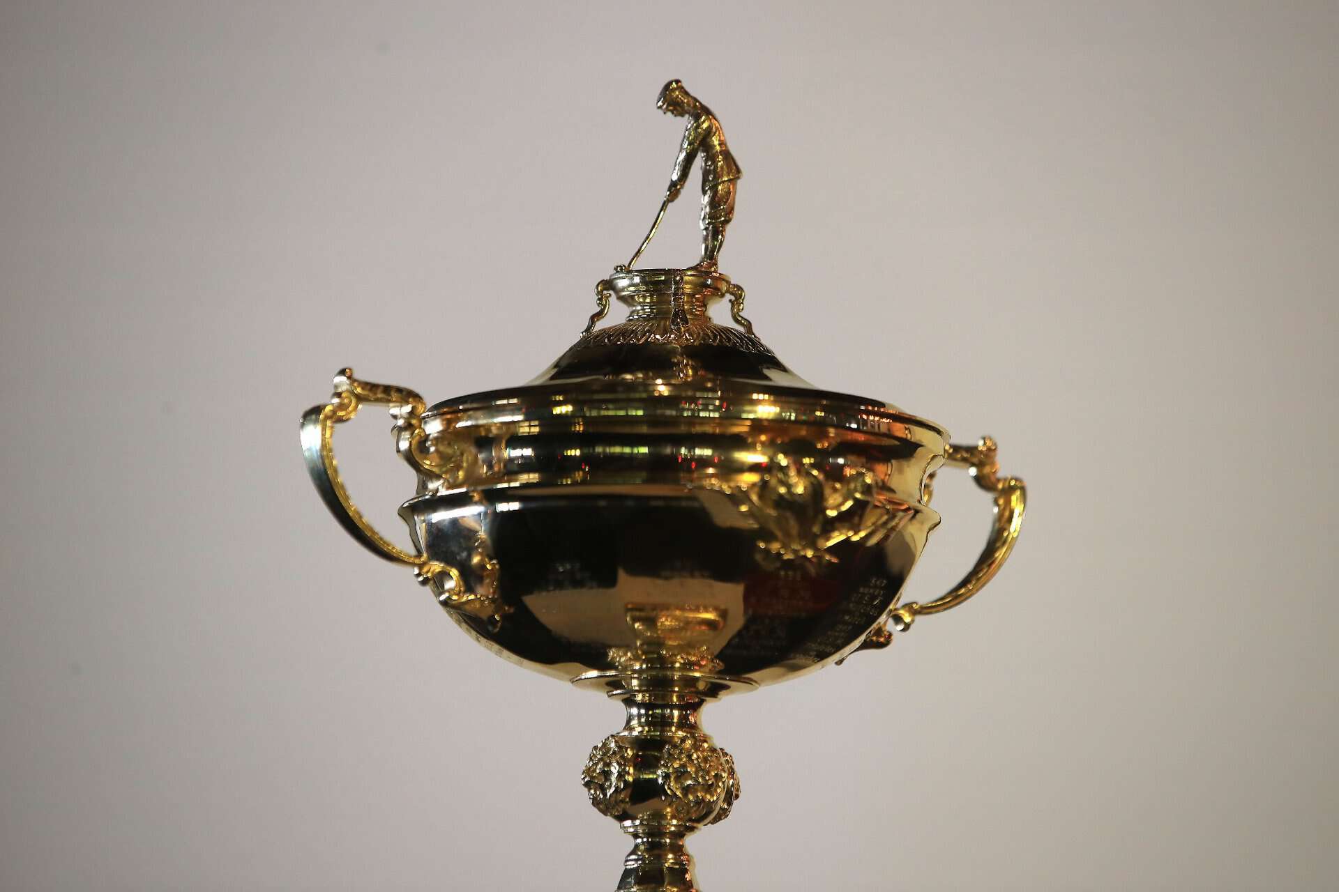 Shiny gold golf trophy with golfer figurine on top, awarded at a prestigious golf event.
