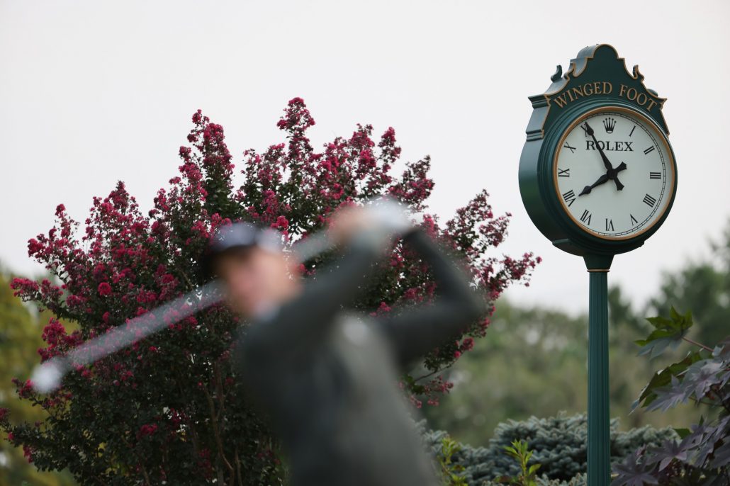 Golfer hitting a tee shot in front of a clock