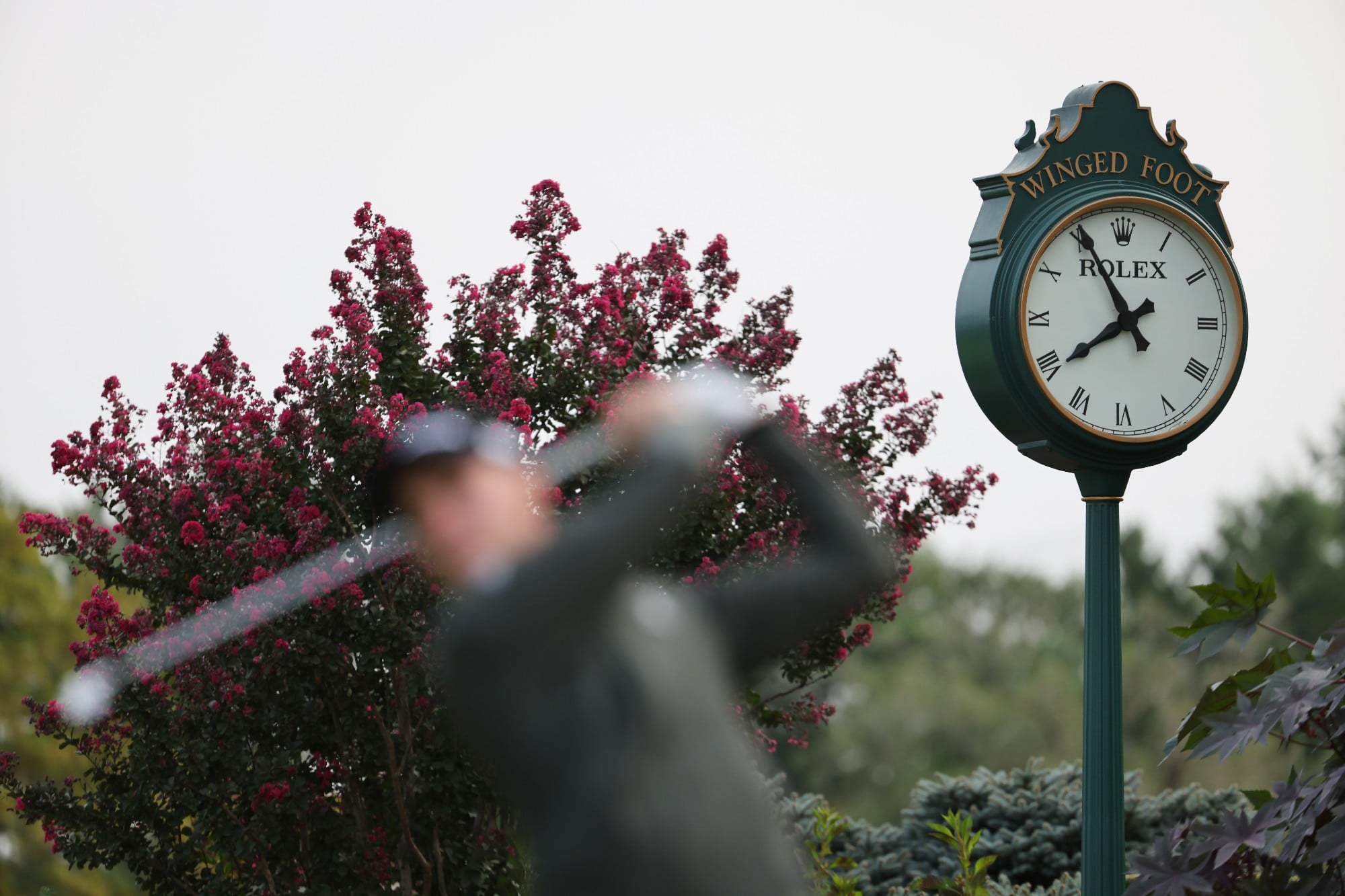 Golfer hitting a tee shot in front of a clock