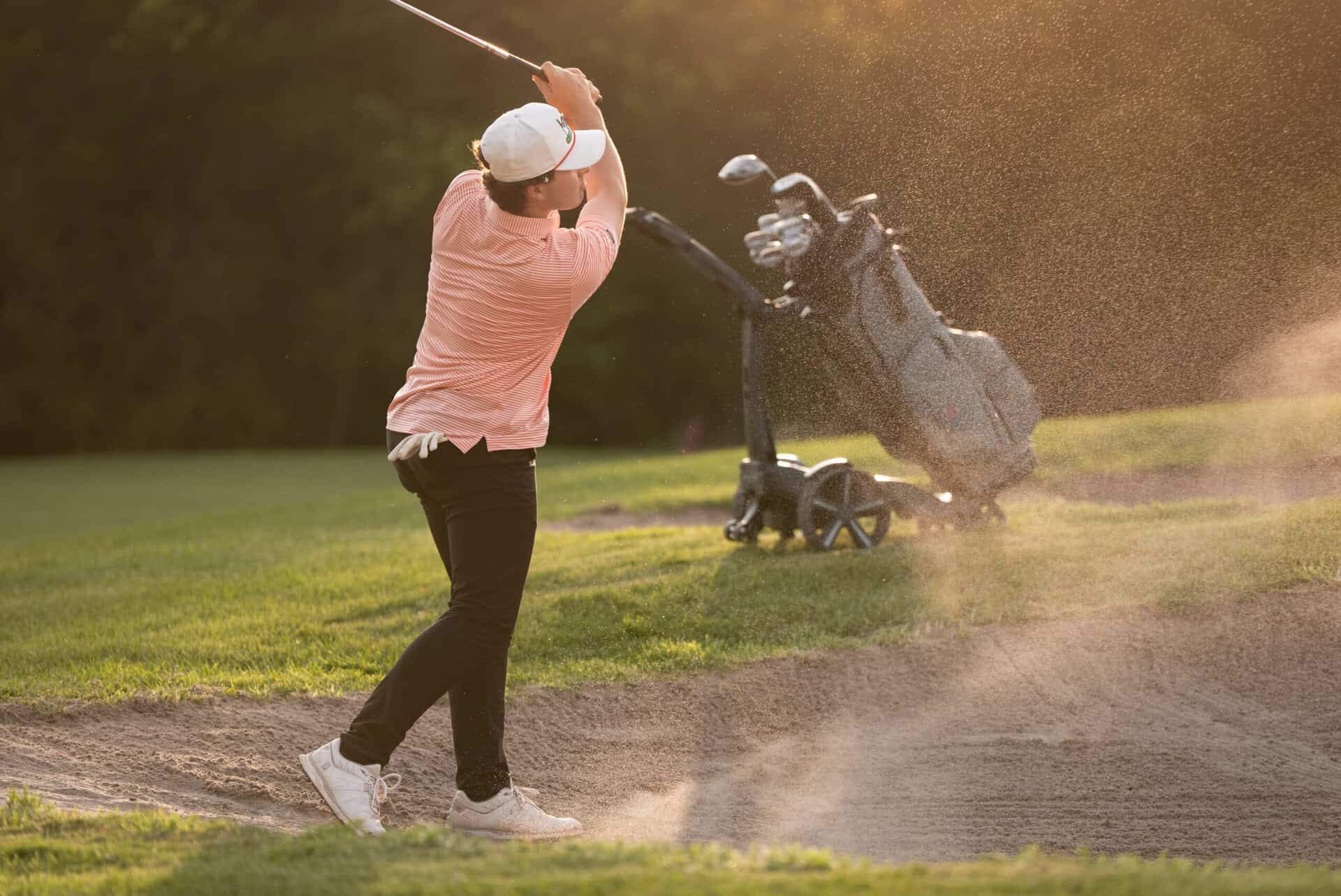 A golfer plays a shot from a bunker with a Stewart Golf trolley in the background | Source: Stewart Golf