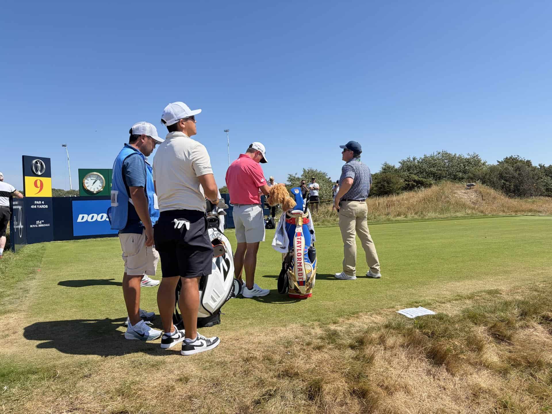 Collin Morikawa studies his yardage book at the 9th tee as a notice tells players about internal out of bounds | Source: NCG