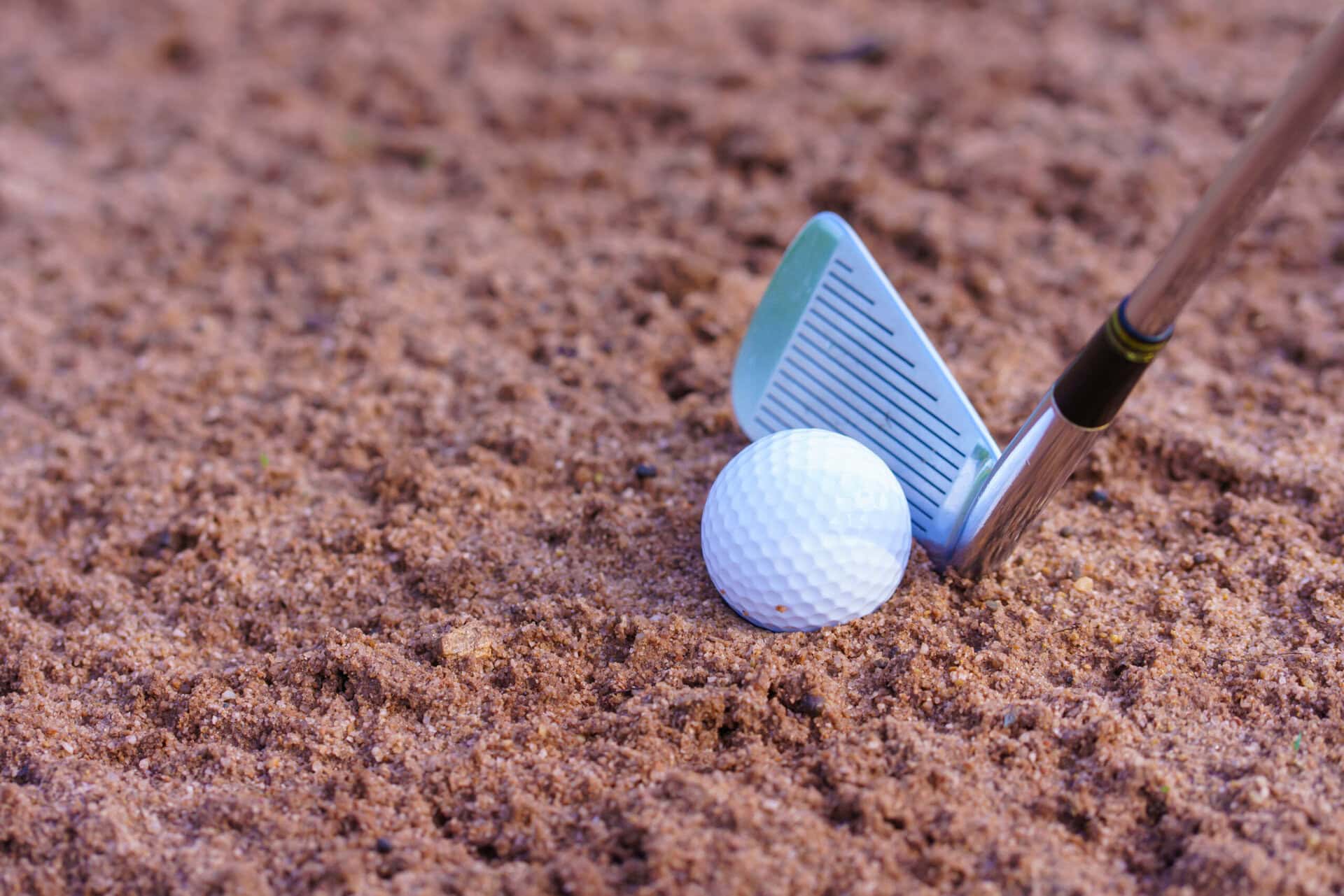 A golf club positioned behind the ball in a bunker | Source: Adobe Stock