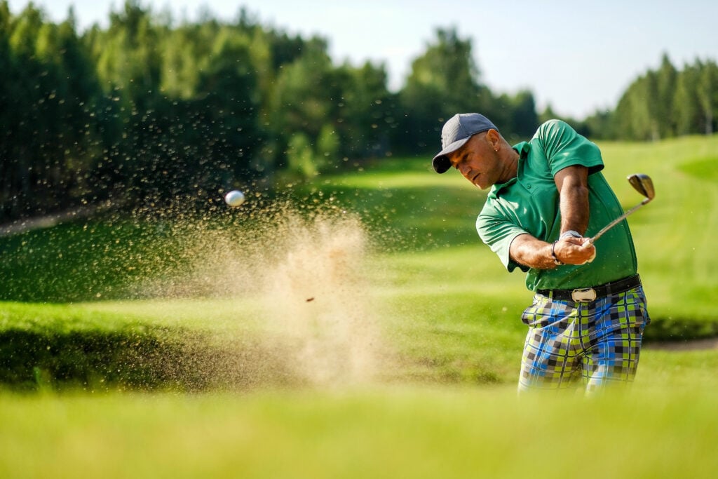 A golfer hits a shot from a bunker | Source: Adobe Stock