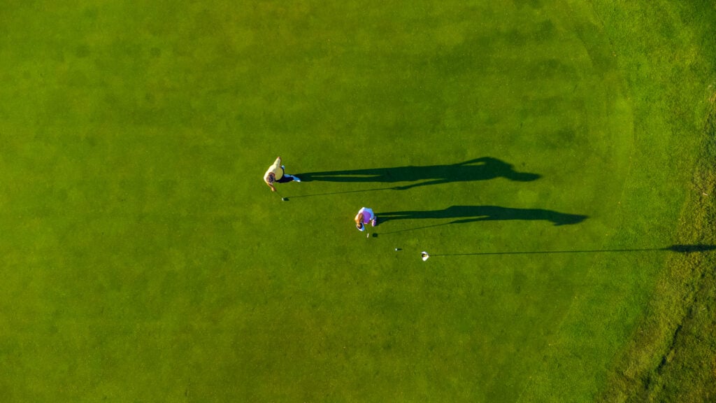 Two golfers playing and casting long shadows on the green | Source: Adobe Stock