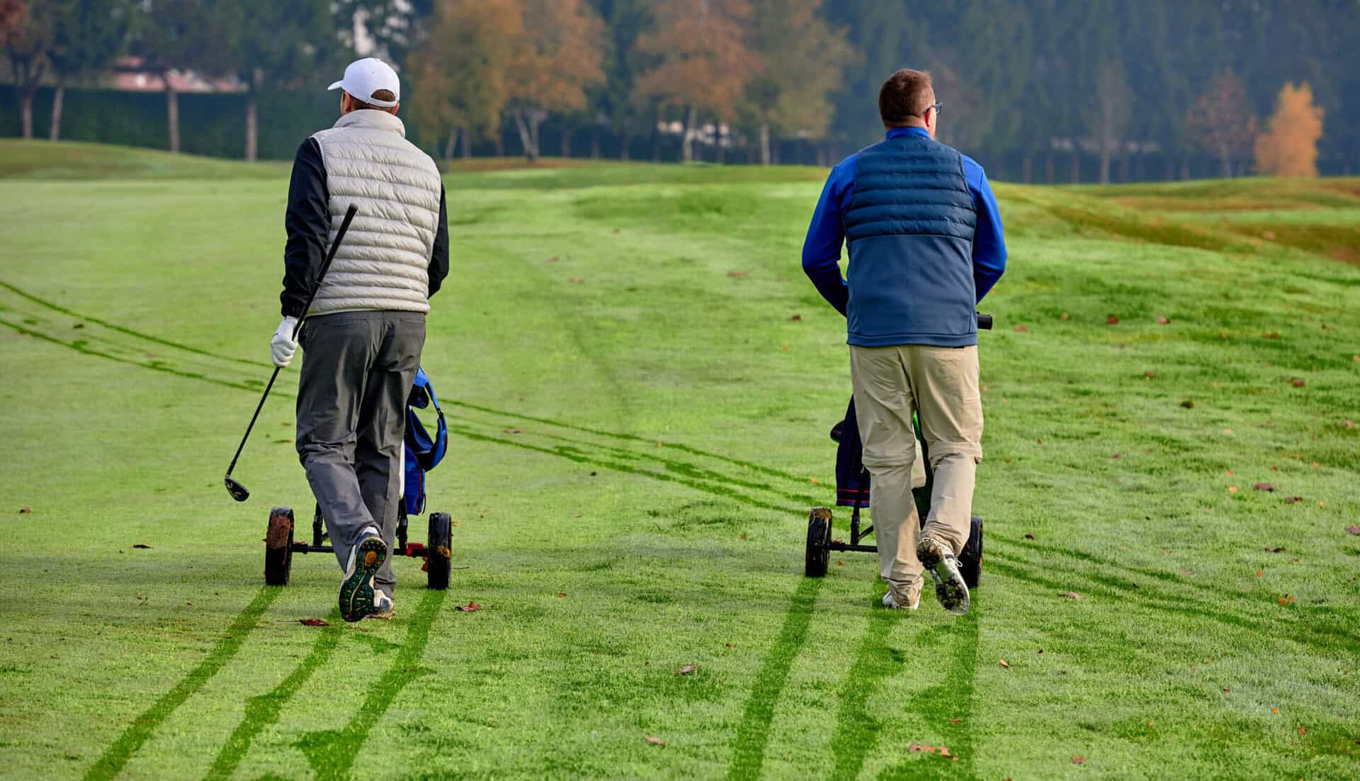 Golfers wheel their trolleys through the dew during winter golf | Source: Adobe Stock