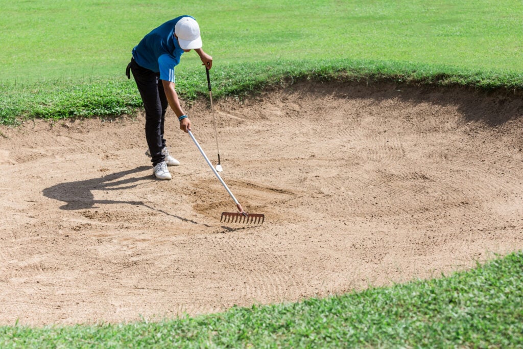 A golfer rakes a bunker | Source: Adobe Stock

raking a bunker rules